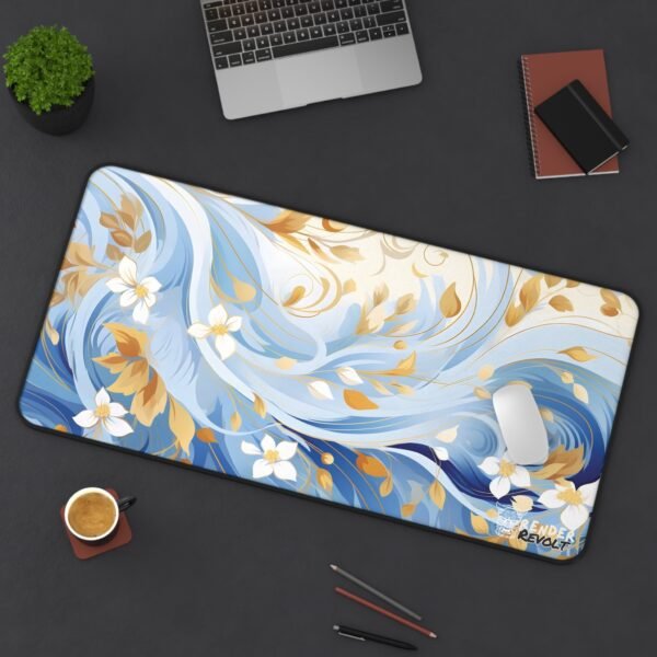 A workstation with a large mouse pad in a flowing blue and gold design, covering most of the wooden desk. The intricate floral pattern, inspired by ocean waves, adds a sense of movement and artistic flair. A wireless mouse sits atop the mat, complementing the setup.